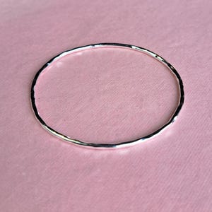 Sterling silver hoola hoop hammered bangle on a pink background