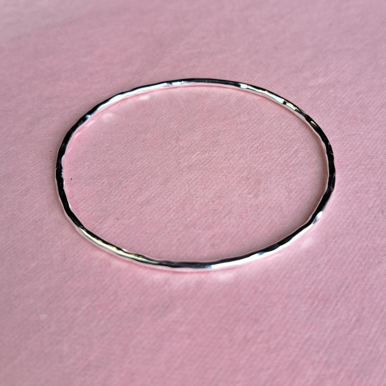 Sterling silver hoola hoop hammered bangle on a pink background
