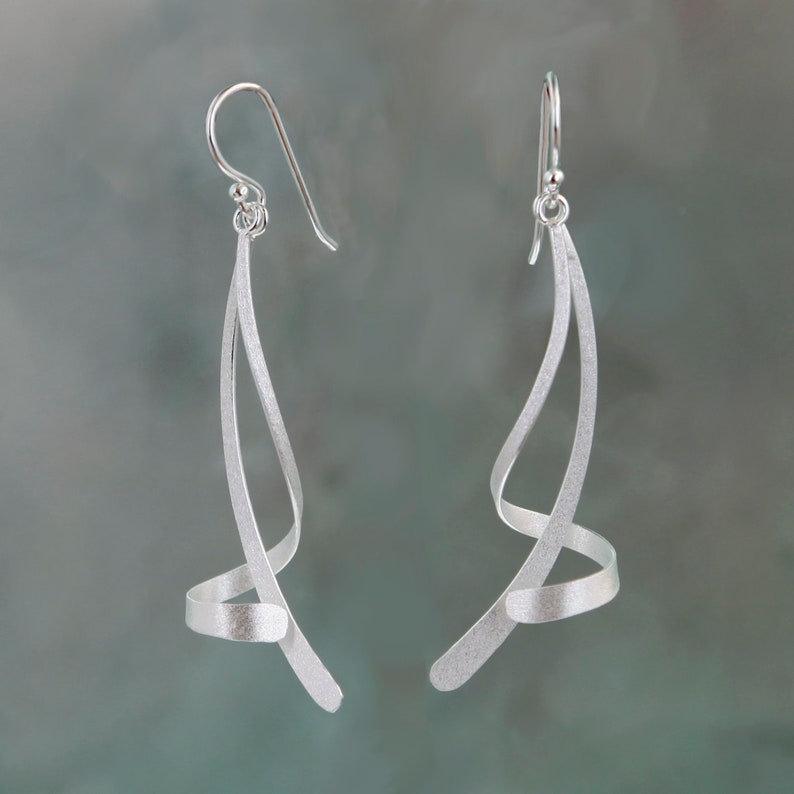 May include: A pair of silver dangle earrings with a twisted, abstract design. The earrings are made of a smooth, brushed metal.