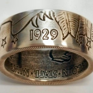 May include: Silver ring made from a 1929 Golden State Mint coin. The ring features a design of feathers and stars.