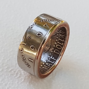 May include: A silver and gold ring made from a half dollar coin. The coin is dated 1999 and has the inscription "In God We Trust" and "Half Dollar" on it.