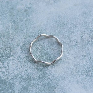 Puede incluir: Un anillo de plata con un diseño ondulado y orgánico. El anillo es simple y elegante.