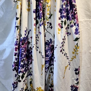 May include: A white maxi skirt with a floral print featuring purple, yellow, and pink flowers. The skirt has a gathered waistband and a flowing silhouette.