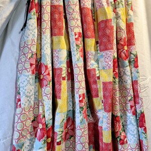 May include: A long, flowing skirt with a patchwork design featuring red, yellow, and blue floral patterns. The skirt has a gathered waistband and a tiered design.