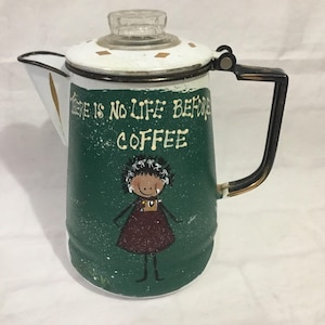 May include: A white and green coffee pot with a black handle. The pot has a glass lid and a painted design of a girl with the text "There is no life before coffee".