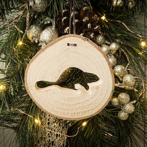 May include: A wooden Christmas bauble shaped like a beaver, hanging on a green Christmas tree with gold and silver decorations.