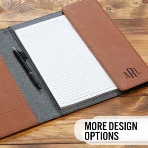 May include: A brown leather portfolio with a gray fabric interior. The portfolio has a pen holder, a notepad, and a flap with the initials "ARL" embossed in black. The portfolio is open and lying on a wooden surface.