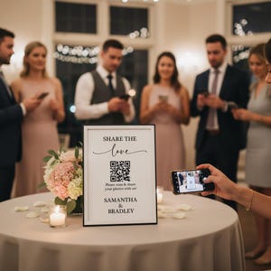 May include: A black framed sign with the words "SHARE THE love" and a QR code, with the names "SAMANTHA & BRADLEY" below. The sign is on a table with flowers and candles, with people in the background.