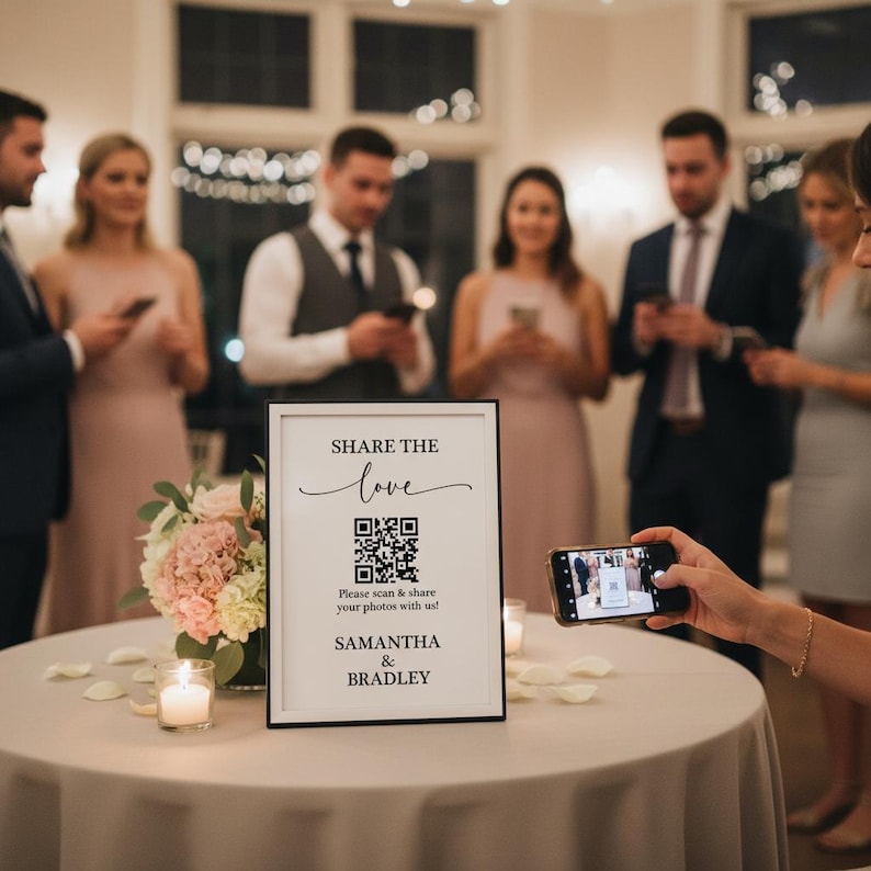 May include: A black framed sign with the words "SHARE THE love" and a QR code, with the names "SAMANTHA & BRADLEY" below. The sign is on a table with flowers and candles, with people in the background.