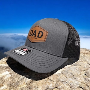 May include: A gray and black trucker hat with a brown leather patch that says "DAD EST. 2008".
