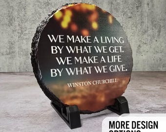 May include: A round, dark grey stone coaster with a colourful sunset image and a white inspirational quote by Winston Churchill: "We make a living by what we get. We make a life by what we give."