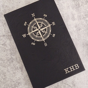 May include: Black leather journal with a compass design and the initials "KHB" embossed in gold.