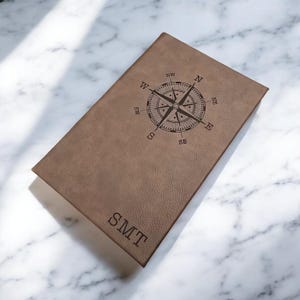 May include: A brown leather journal with a compass design and the initials "SMT" engraved on the cover.