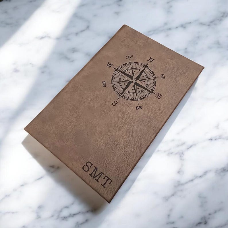 May include: A brown leather journal with a compass design and the initials "SMT" engraved on the cover.
