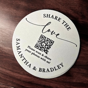 May include: A white round paper coaster with black text that says "Share the love" and a QR code. Below the QR code is the text "Please scan & share your photos with us!" and "Samantha & Bradley".