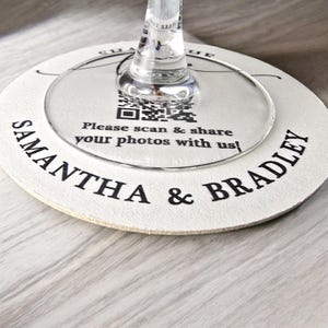 May include: White round coaster with the text "Samantha & Bradley" printed in black. A clear glass circle with a QR code and the text "Please scan & share your photos with us!" is on top of the coaster.