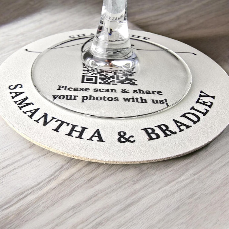 May include: White round coaster with the text "Samantha & Bradley" printed in black. A clear glass circle with a QR code and the text "Please scan & share your photos with us!" is on top of the coaster.