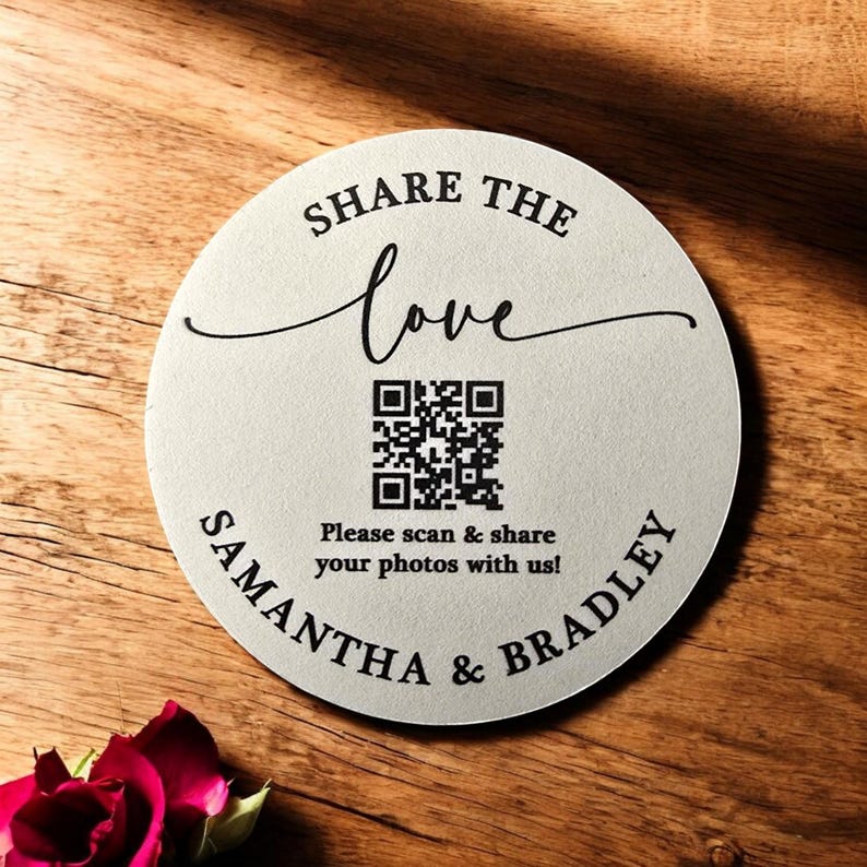 May include: A round, white, wooden sign with black text that reads "Share the love" in a cursive font. A black and white QR code is below the text, with the text "Please scan & share your photos with us!" below the QR code. The text "Samantha & Bradley" is written in a circular arc around the bottom of the sign.