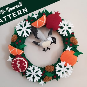 May include: A felt Christmas wreath with a bird, oranges, pomegranates, pine cones, and snowflakes. The wreath is green with red berries and white stars. The text "Sew-It-Yourself PATTERN" is at the top of the image.
