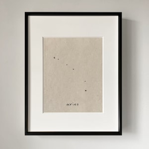 Peut inclure: Une impression encadrée en noir avec un passe-partout blanc. L'impression présente un dessin au trait simple de la constellation du Bélier avec le mot "aries" écrit en dessous.