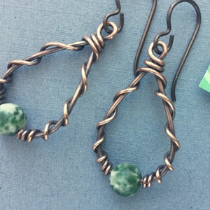 May include: A pair of copper wire earrings with green and white agate stones. The earrings are teardrop shaped and have a twisted wire design.