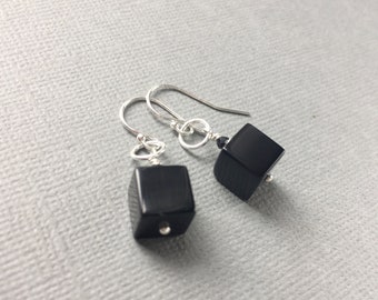 May include: A pair of silver earrings with black square-shaped gemstone drops.