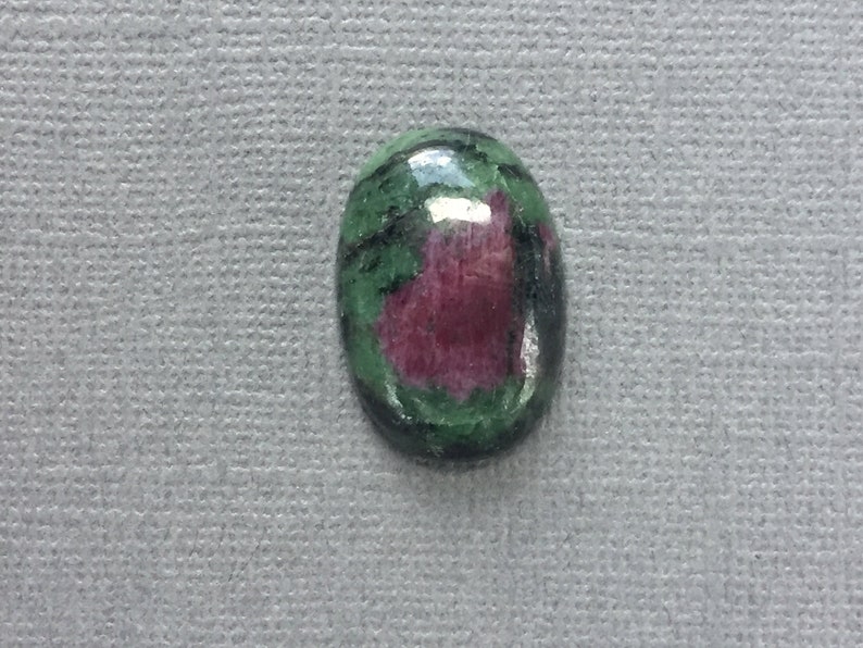 May include: Oval-shaped green and pink gemstone cabochon with a smooth, polished surface.