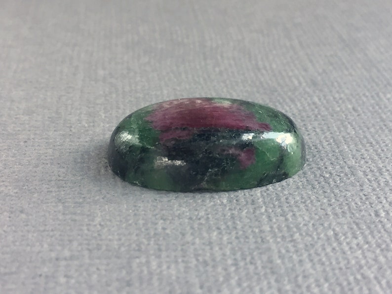 May include: Oval-shaped green and pink gemstone cabochon with a smooth, polished surface.