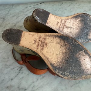 May include: A pair of brown leather Valentino sandals, size 38, with a wedge heel. The soles are worn and show signs of use. The sandals have a strap design and are made in Italy.