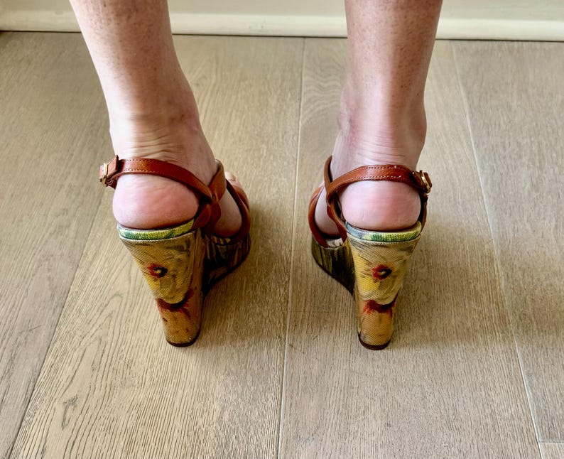 May include: Brown leather wedge sandals with floral print on the wedge heel. The sandals have a strap around the ankle and a strap across the toes. The heels are approximately 4 inches high.
