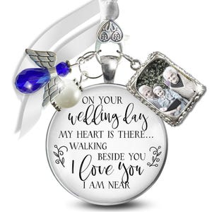 May include: A round, silver-toned wedding ornament with a photo charm and a blue angel charm. The ornament has the text "ON YOUR wedding day, MY HEART IS THERE... WALKING BESIDE YOU I LOVE YOU I AM NEAR."