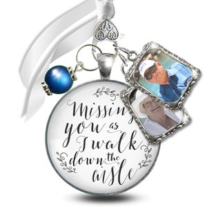 May include: A white satin ribbon with a silver charm that says "Missing you as I walk down the aisle". The charm has two small photo frames with pictures of an older couple. The charm is attached to a blue bead.