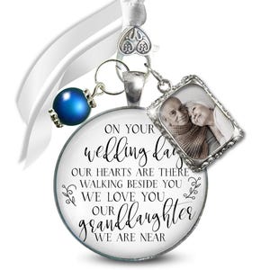 May include: A wedding day pendant with a photo of an elderly couple, a blue bead, and a white ribbon. The pendant has the text "ON YOUR wedding day OUR HEARTS ARE THERE WALKING BESIDE YOU WE LOVE YOU OUR granddaughter WE ARE NEAR."