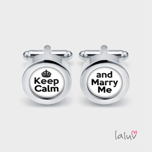 Puede incluir: Un par de gemelos de plata con fondo blanco. Un gemelo dice "Keep Calm" con una corona sobre el texto. El otro gemelo dice "and Marry Me".