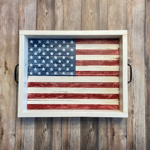 May include: A white wooden tray with black handles features a painted American flag design. The flag is red, white, and blue with a distressed look.