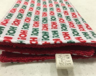 May include: A folded red and white kitchen towel with a green and red "Ho Ho Ho" pattern. The towel has a frayed edge and a small white tag that says "taybr SEWN".