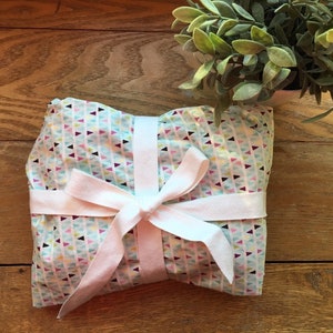 Peut inclure: Un cadeau emballé dans un tissu bleu et blanc avec un motif géométrique de triangles. Le tissu est noué avec un ruban blanc.