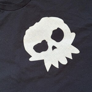 Puede incluir: Camiseta negra con un dise&ntilde;o de calavera blanca. La calavera es un dise&ntilde;o sencillo y estilizado, colocado en el centro. La camiseta tiene cuello redondo y mangas cortas, adecuada para el uso diario.