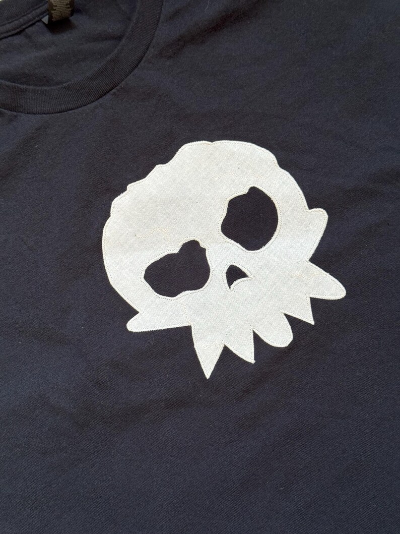 Puede incluir: Camiseta negra con un dise&ntilde;o de calavera blanca. La calavera es un dise&ntilde;o sencillo y estilizado, colocado en el centro. La camiseta tiene cuello redondo y mangas cortas, adecuada para el uso diario.