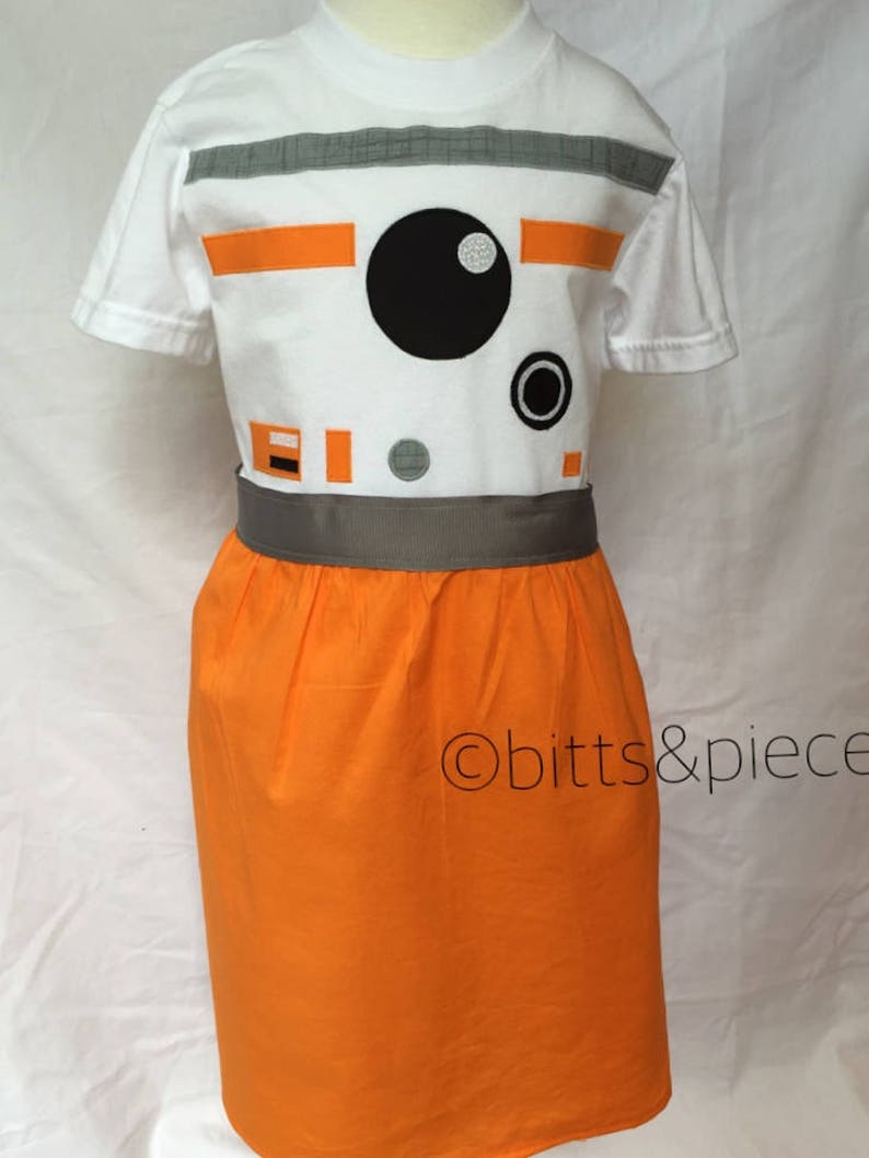 May include: A white t-shirt with an orange and gray BB-8 design. The shirt is paired with an orange skirt and a gray belt. The text "obitt&piece" is visible on the skirt.