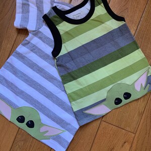 Pode incluir: Duas camisas listradas com um gr&aacute;fico de personagem verde. A camisa &agrave; esquerda &eacute; branca e cinza com mangas curtas. A camisa &agrave; direita &eacute; verde, cinza e branca sem mangas. Ambas as camisas t&ecirc;m um personagem verde com olhos grandes e orelhas cor-de-rosa.