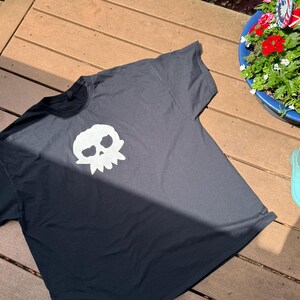 Puede incluir: Camiseta negra con un dise&ntilde;o de calavera blanca. El dise&ntilde;o de la calavera est&aacute; centrado en la parte delantera de la camiseta. La camiseta es de manga corta.