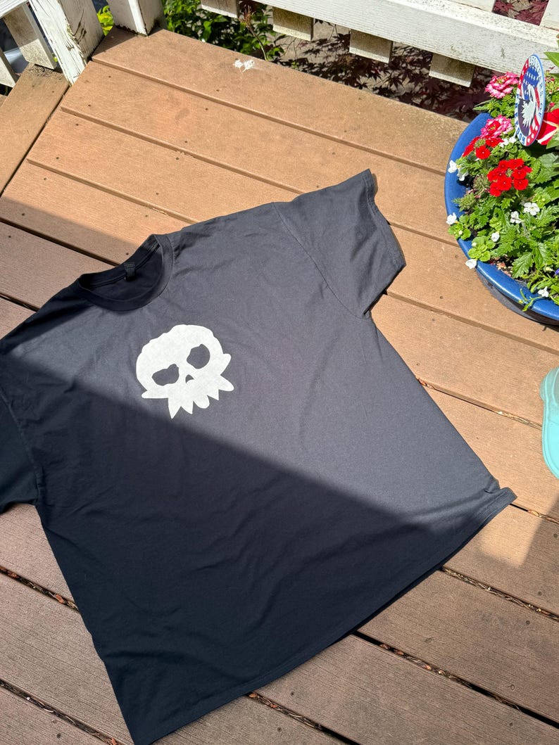 Puede incluir: Camiseta negra con un dise&ntilde;o de calavera blanca. El dise&ntilde;o de la calavera est&aacute; centrado en la parte delantera de la camiseta. La camiseta es de manga corta.