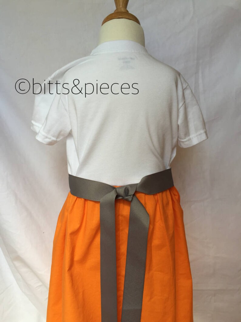 May include: A white t-shirt with a gray sash tied around the waist, worn over an orange skirt. The skirt is gathered at the waist and has a full, flowing shape.