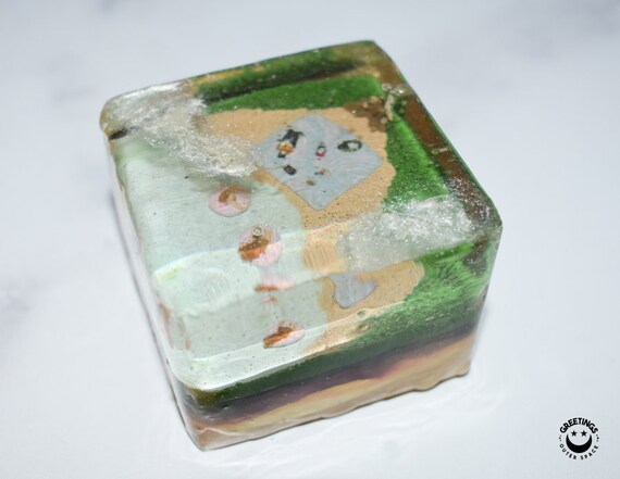 A sculptor hand-builds a layered cross-section of YOUR specific plot of earth — soil strata, roots, rocks — in polymer clay and epoxy resin; genuinely one-of-a-kind micro-geology art.