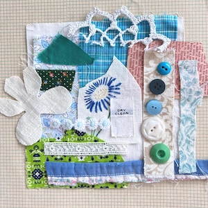 May include: A textile collage featuring assorted fabric scraps in blue, green, and white, including a white flower cutout, a blue embroidered daisy, a white lace trim, and a vertical strip with five buttons. A small white tag reads DRY CLEAN.