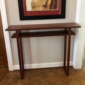 May include: A dark wood console table with a single shelf. The table has a simple, modern design with clean lines and a rectangular shape. The table is 30 inches tall and 40 inches wide.