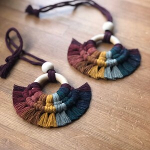 May include: Two handmade macrame necklaces with wooden beads and colorful fringe. The necklaces are made with a variety of colors, including burgundy, brown, yellow, gray, and teal.