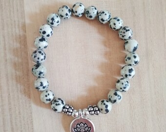 May include: A bracelet made of white and black speckled beads with a silver lotus flower charm.