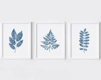 Può includere: Set di tre stampe ad acquerello blu con diversi motivi di foglie. Le stampe sono incorniciate in cornici bianche e sono esposte su una parete bianca.